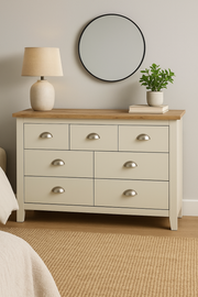 Lavish Kitchen Isle cream chest of 7 drawers with oak effect top and steel handles in a bedroom setting.